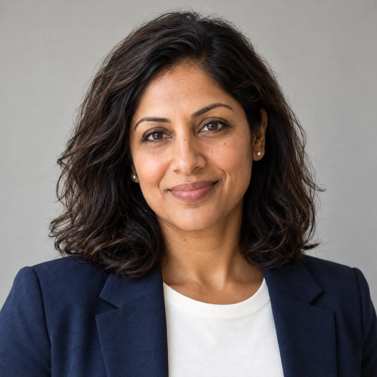 Aisha mit marineblauem Blazer vor neutralem Hintergrund — fiktives KI-Beispiel.